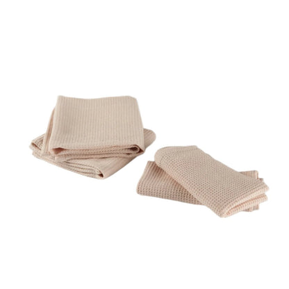 Two stacks of light pink waffle-textured cotton kitchen towels displayed on a white background. One stack shows folded towels, while the other shows towels loosely arranged to showcase their texture.